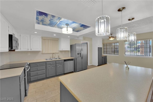 kitchen with a sink, a ceiling fan, a raised ceiling, gray cabinetry, and appliances with stainless steel finishes