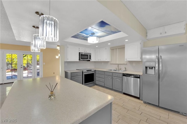 kitchen featuring french doors, a sink, stainless steel appliances, gray cabinets, and a raised ceiling