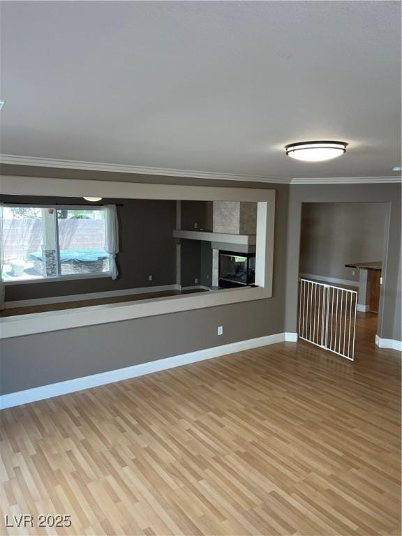 10974 Fintry Hills St, Las Vegas, NV 89141 - unfurnished living room with light wood-style floors, ornamental molding, baseboards, and a glass covered fireplace
