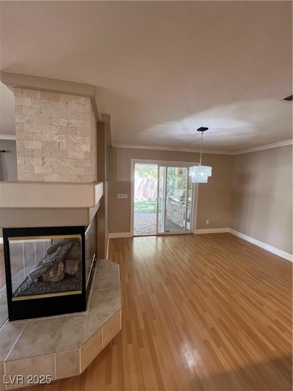 10974 Fintry Hills St, Las Vegas, NV 89141 - unfurnished living room featuring a multi sided fireplace, wood finished floors, baseboards, a chandelier, and ornamental molding