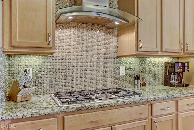 kitchen featuring exhaust hood, backsplash, light brown cabinetry, light stone counters, and stainless steel gas stovetop