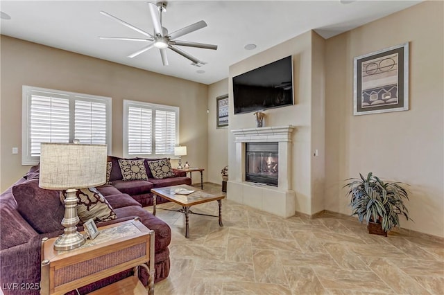 living room featuring a tiled fireplace, a ceiling fan, and baseboards