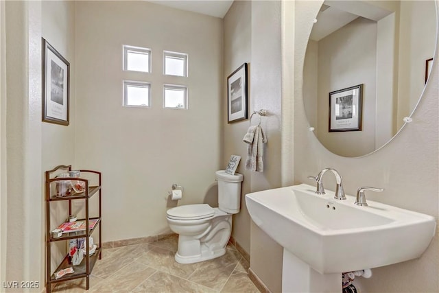 half bathroom with baseboards, a sink, and toilet