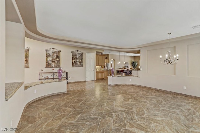 unfurnished living room featuring a raised ceiling, visible vents, and a chandelier