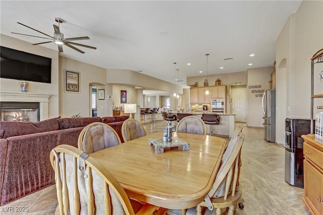 dining space featuring a ceiling fan, arched walkways, and a glass covered fireplace