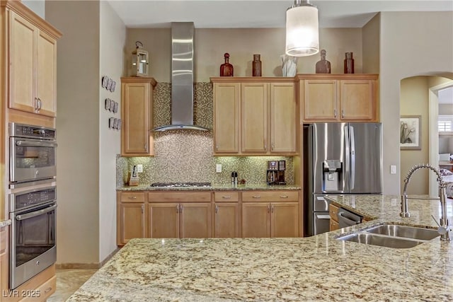 kitchen with wall chimney range hood, a sink, arched walkways, stainless steel appliances, and decorative backsplash