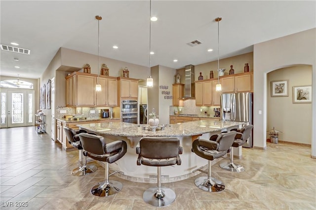 kitchen featuring wall chimney range hood, backsplash, stainless steel appliances, and visible vents