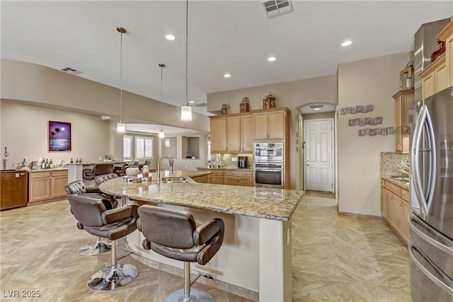 kitchen with a kitchen breakfast bar, visible vents, light brown cabinetry, a sink, and stainless steel appliances
