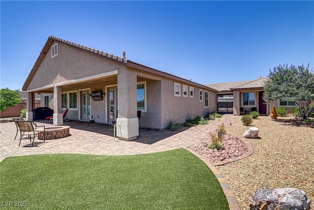 rear view of property featuring a lawn, a patio area, fence, an outdoor fire pit, and stucco siding