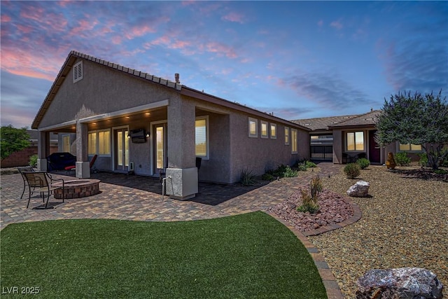 back of property at dusk featuring a patio, an outdoor fire pit, stucco siding, and a lawn