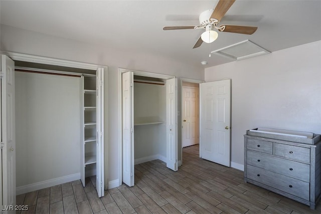 unfurnished bedroom with multiple closets, light wood-style flooring, attic access, a ceiling fan, and baseboards