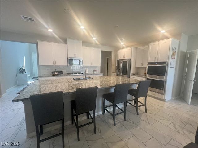 7527 Ardenno St, North Las Vegas, NV 89084 - kitchen featuring stainless steel appliances, light marble finish flooring, white cabinets, a breakfast bar, and tasteful backsplash