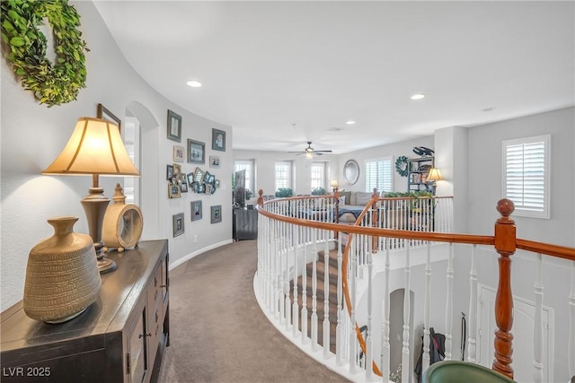 hallway featuring carpet floors, arched walkways, recessed lighting, baseboards, and an upstairs landing