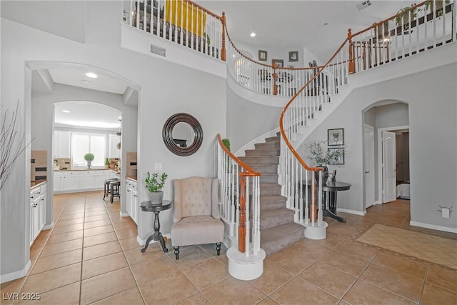 stairway featuring visible vents, arched walkways, tile patterned floors, baseboards, and a high ceiling