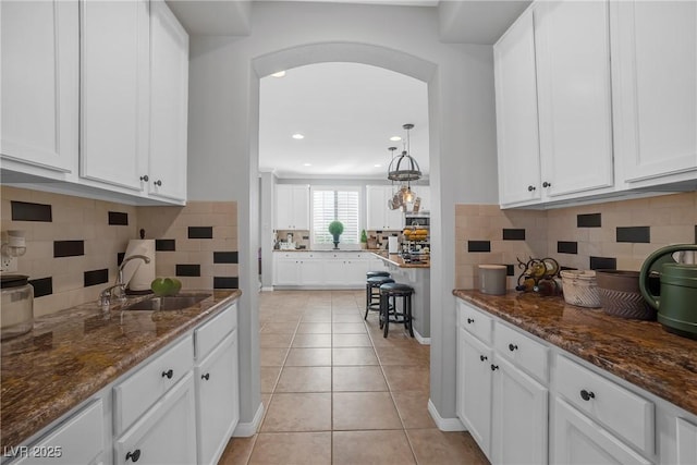 kitchen with white cabinets, light tile patterned flooring, a sink, arched walkways, and dark stone countertops