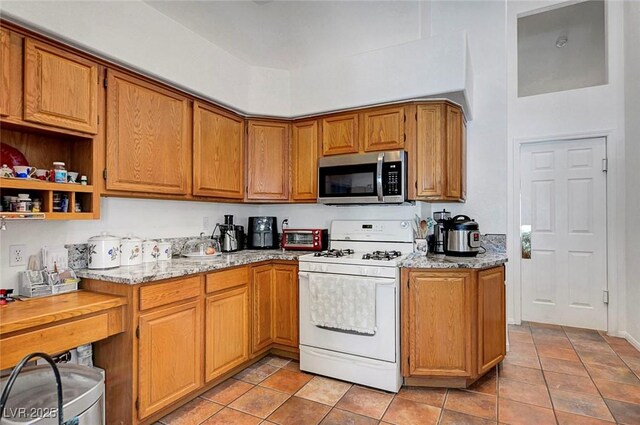 7874 Trail Boss Ct, Las Vegas, NV 89113 - kitchen featuring stainless steel microwave, white gas stove, light tile patterned flooring, light stone counters, and brown cabinets