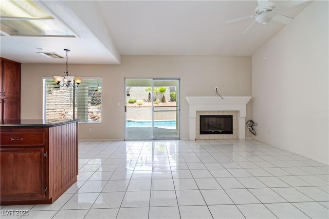 unfurnished living room with visible vents, a tiled fireplace, light tile patterned floors, and ceiling fan with notable chandelier