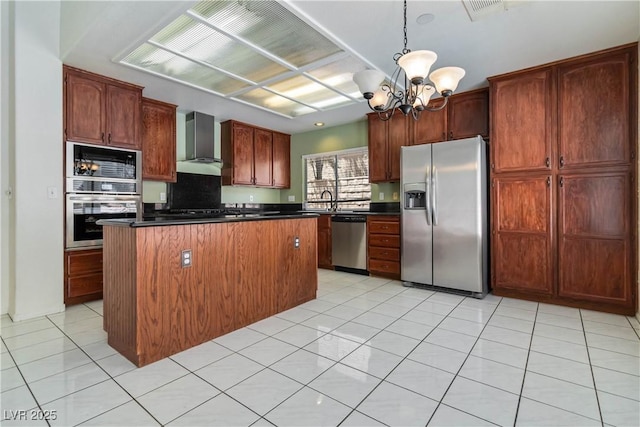 kitchen featuring wall chimney range hood, a kitchen island, appliances with stainless steel finishes, dark countertops, and a chandelier