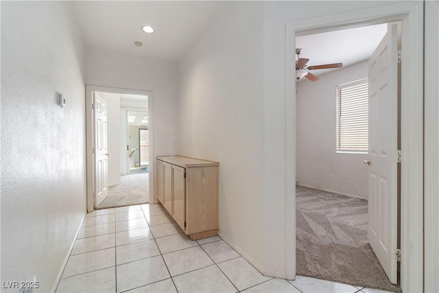 corridor featuring baseboards, light tile patterned flooring, and light colored carpet