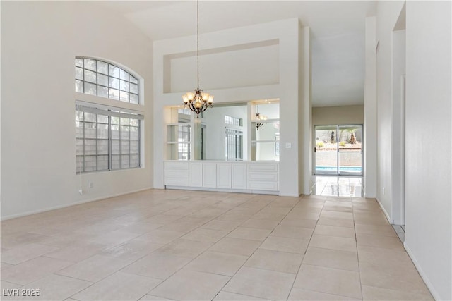 spare room featuring an inviting chandelier, light tile patterned floors, baseboards, and a towering ceiling