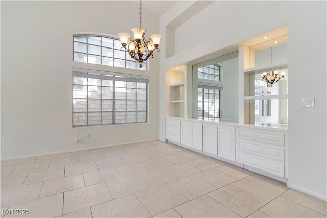 unfurnished dining area with light tile patterned floors, a towering ceiling, baseboards, and a notable chandelier