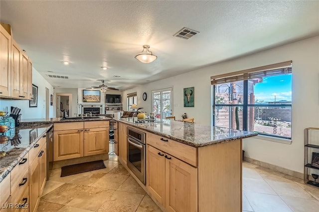 kitchen with a peninsula, light brown cabinetry, stainless steel oven, ceiling fan, and dark stone countertops