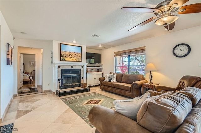 living room with ceiling fan, visible vents, a tile fireplace, light tile patterned floors, and baseboards