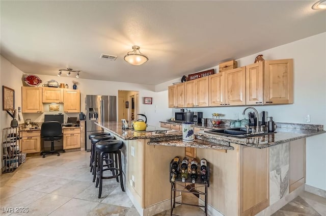 kitchen with a breakfast bar area, stainless steel refrigerator with ice dispenser, light brown cabinetry, a sink, and a peninsula