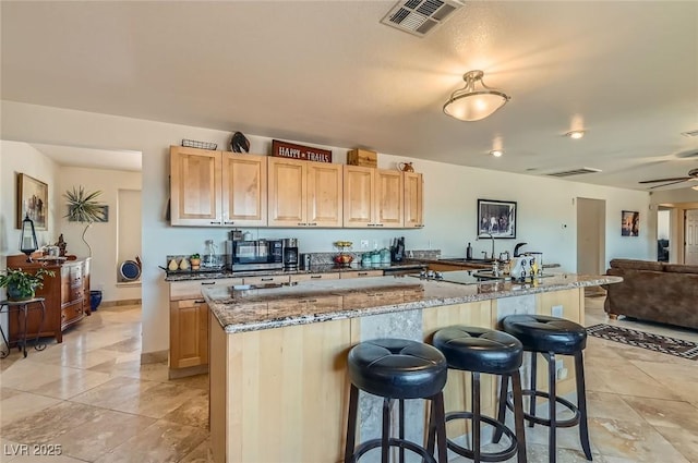 kitchen with visible vents, light brown cabinetry, a breakfast bar area, stainless steel microwave, and light stone counters
