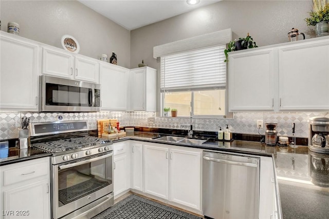 kitchen with dark countertops, appliances with stainless steel finishes, a sink, white cabinetry, and decorative backsplash
