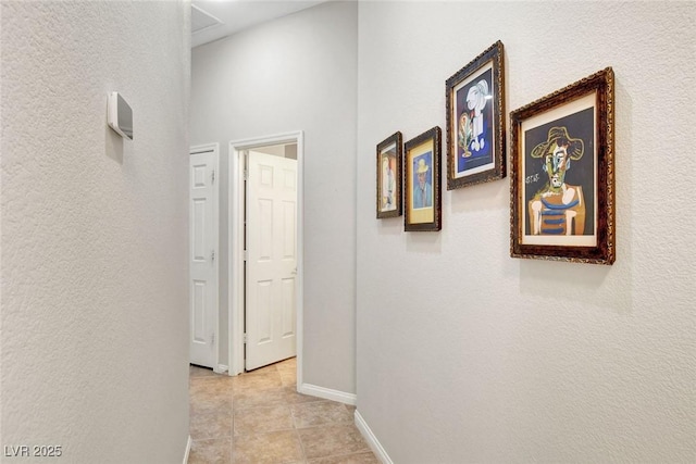 corridor featuring baseboards, a textured wall, and light tile patterned floors