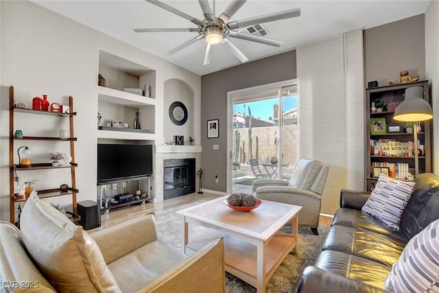 living room featuring built in features, ceiling fan, wood finished floors, and a tile fireplace