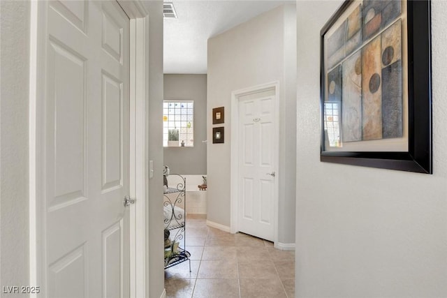 hall featuring light tile patterned floors, baseboards, and visible vents