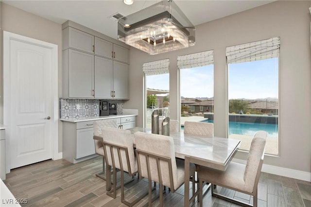 dining room with a notable chandelier, baseboards, visible vents, and wood finished floors