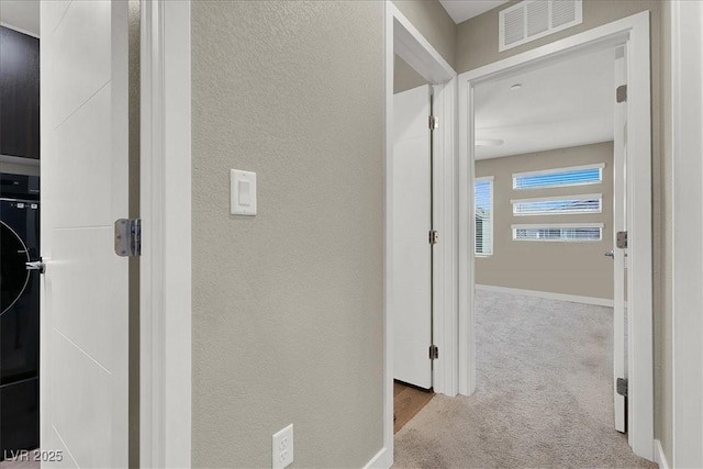 hall featuring visible vents, carpet flooring, a textured wall, and baseboards