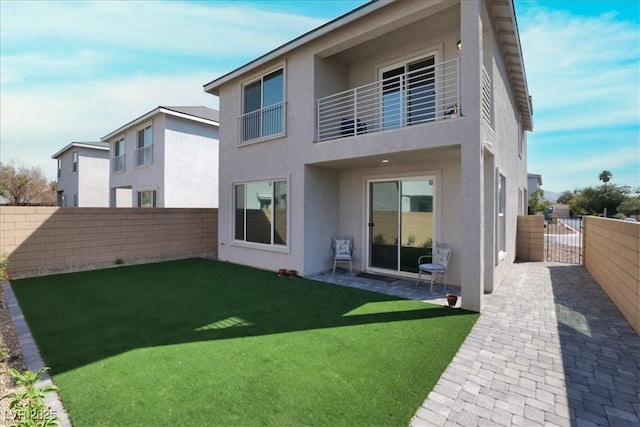 rear view of house featuring a fenced backyard, stucco siding, a balcony, and a gate