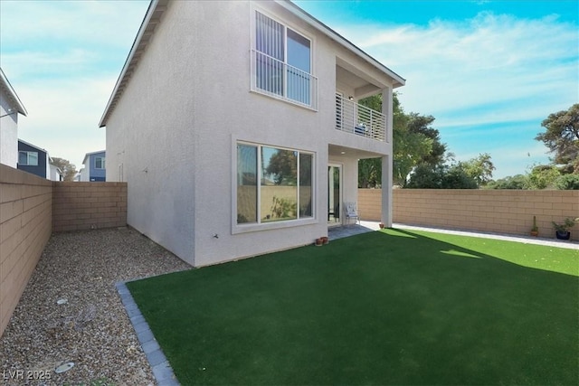 back of property featuring a lawn, a balcony, a fenced backyard, and stucco siding