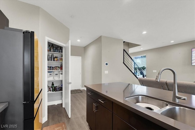 kitchen with freestanding refrigerator, dark brown cabinetry, recessed lighting, a sink, and light wood-style flooring