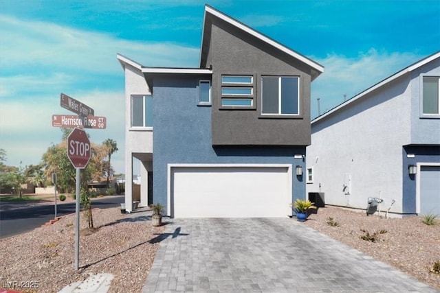 contemporary house featuring an attached garage, cooling unit, decorative driveway, and stucco siding