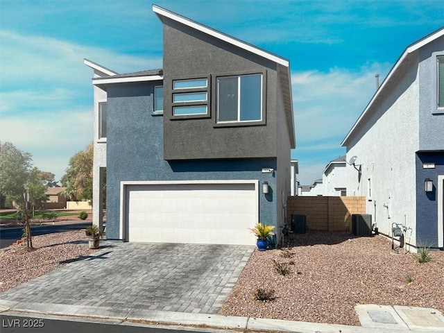 view of front of house with an attached garage, central AC, stucco siding, and fence