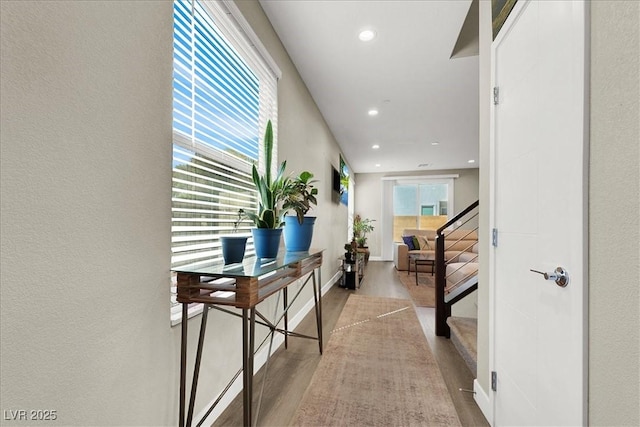 hallway with stairs, wood finished floors, baseboards, a textured wall, and recessed lighting