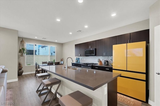 kitchen featuring dark countertops, a breakfast bar, an island with sink, a sink, and appliances with stainless steel finishes