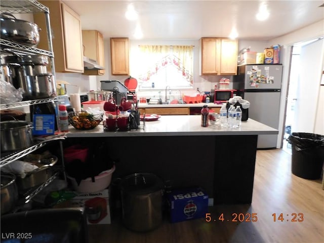 kitchen with freestanding refrigerator, a peninsula, light brown cabinets, a sink, and light wood-style flooring