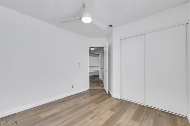 unfurnished bedroom featuring a closet, a textured ceiling, a ceiling fan, and light wood-style floors