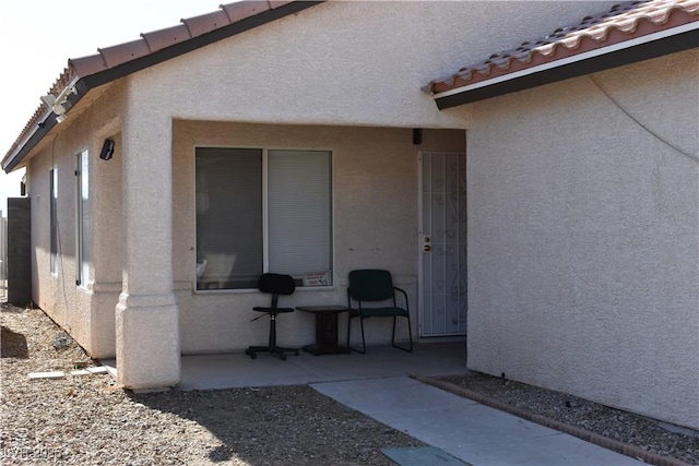 view of exterior entry featuring a tiled roof, a patio area, and stucco siding