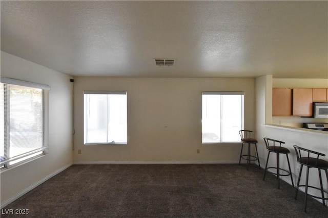 living room featuring visible vents, baseboards, a wealth of natural light, and dark colored carpet