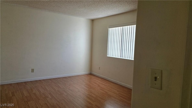 spare room with a textured ceiling, baseboards, and wood finished floors