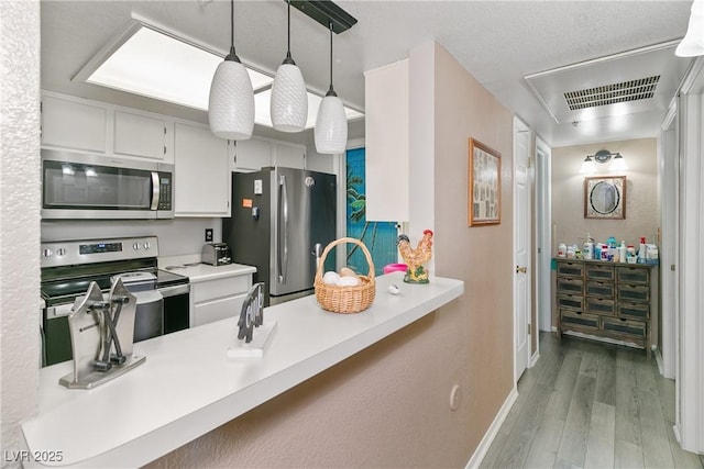 kitchen with stainless steel appliances, baseboards, a peninsula, wood finished floors, and visible vents