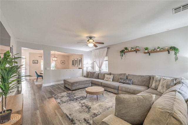 living area featuring baseboards, ceiling fan with notable chandelier, wood finished floors, and visible vents