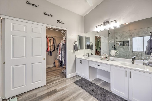 bathroom featuring double vanity, a tile shower, a sink, and wood finished floors